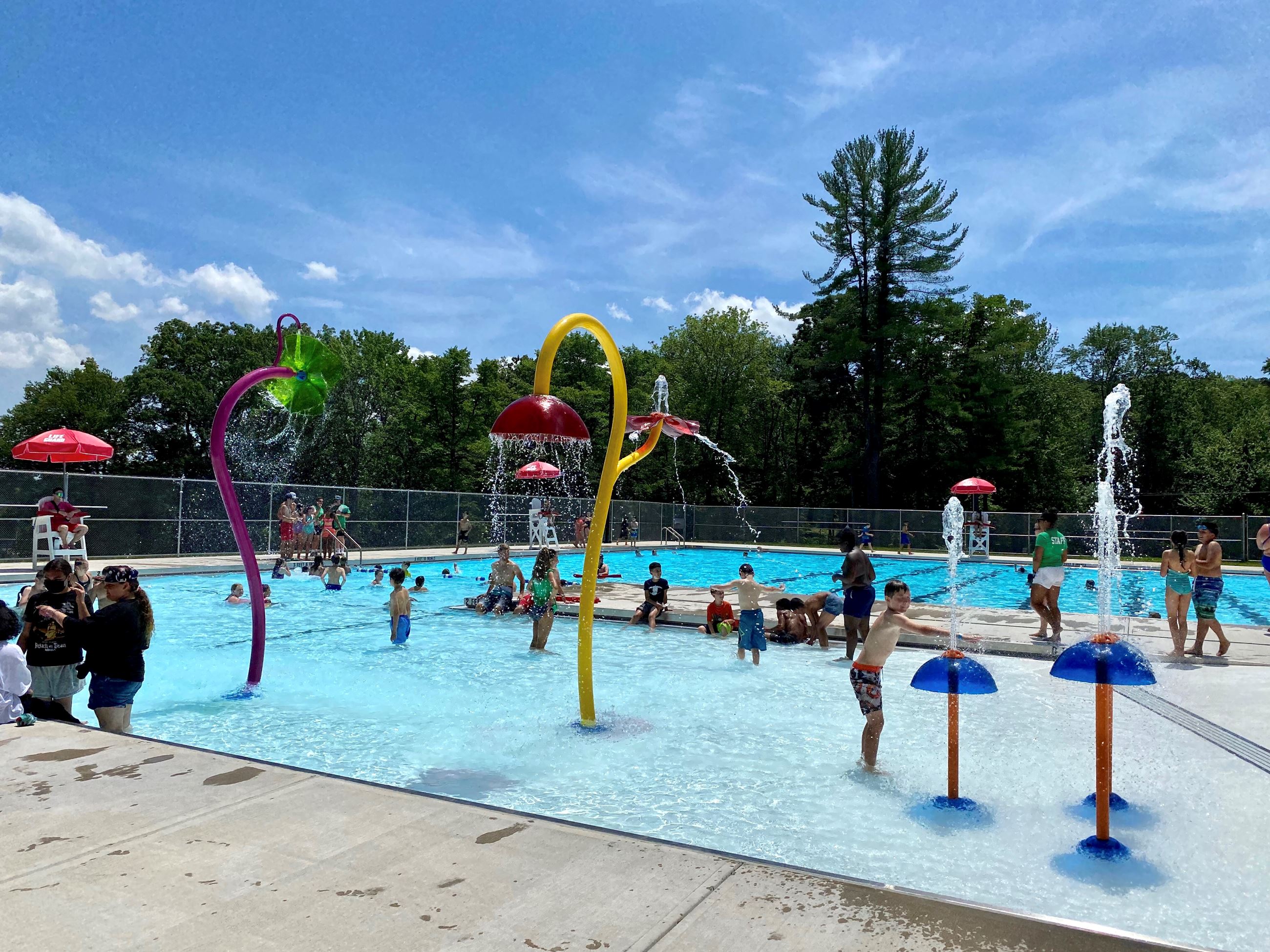 Children and families swimming in an outdoor pool with a zero-depth entry featuring spray feature. 